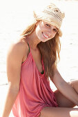 A young blonde woman on a beach wearing a pink top and a beige hat