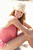 A young blonde woman on a beach wearing a pink top and a beige hat