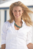 A young blonde woman on a beach wearing a white blouse and a chunky necklace
