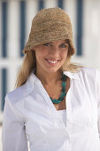 A young blonde woman on a beach wearing a white blouse and a brown hat
