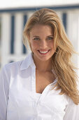 A young blonde woman on a beach wearing a white blouse