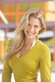 A young blonde woman on a beach wearing an olive top