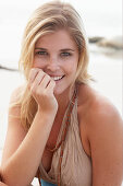 A blonde woman on a beach wearing a beige summer dress