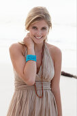 A blonde woman on a beach wearing a beige summer dress