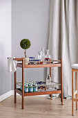 Simple serving trolley with drinks in front of a grey wall