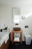 Stone washbasin on wooden washstand in bathroom with slate floor tiles