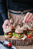 Hands putting small burgers on a wooden plate