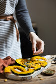 Woman flavouring pumpkin slices with origan and rosemary