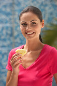 A young brunette woman wearing a pink top and holding a slice of pineapple