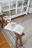Holzbank mit Buch und Teetassen vor weißem Vitrinenschrank