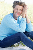 Reife Frau mit blonder Kurzhaarfrisur in Bluejeans und blauem Pullover über weißem Shirt in der Natur