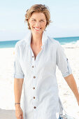 A mature woman with short blonde hair on a beach wearing a striped shirt