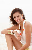 A brunette woman on a beach wearing a white top and shorts