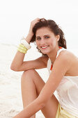 A brunette woman on a beach wearing a white top and shorts