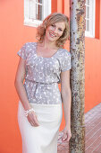 A blonde woman wearing a grey spotted blouse and a white skirt