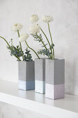 Concrete-effect vases handmade from milk cartons holding ranunculus on shelf