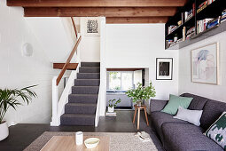 Graues Polstersofa im Wohnraum mit Holzbalkendecke und Treppenaufgang
