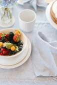 Bowl of berries and cape gooseberries on table with linen tablecloth
