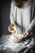 Woman making dough and pouring beaten egg into bowl with flour while making dough