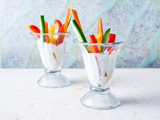 Sliced zucchini, red, green and yellow bell pepper and carrot in glass cups filled with creamy ranch dressing