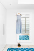 Summer dress on wall mirror, blue carpet and wardrobe in white bedroom