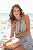 A young brunette woman on a beach wearing a beige summer dress and a necklace