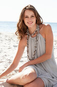 A young brunette woman on a beach wearing a beige summer dress and a necklace