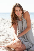 A young brunette woman on a beach wearing a beige summer dress and a necklace