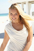 A blonde woman on a beach wearing a beige summer dress