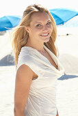 A blonde woman on a beach wearing a beige summer dress