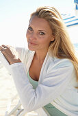 Blonde Frau in türkisem Top und weißer Jacke am Strand