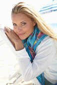 A blonde woman on a beach wearing a colourful scarf and a white jacket