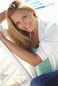 A blonde woman on a beach wearing a turquoise top and a white jacket