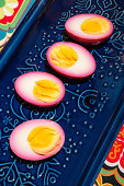 Eggs pickled in beetroot, halved, on a blue ceramic plate