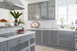 Kitchen counter with pale grey cupbards, wall cabinets with glass doors and extractor hood above worksurface with hob in foreground