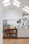Island counter running into shelves in white kitchen with skylights