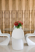 White designer chairs around glass table in front of wood-clad wall