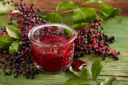 Homemade strawberry and elderberry jam in a glass on a green wooden surface