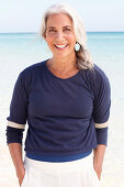A mature woman with white hair on a beach wearing a blue top and white shorts