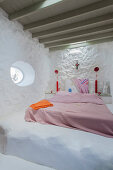 Double bed with pink covers in rustic bedroom with whitewashed walls