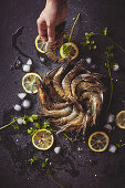 Fresh Tiger Prawns and lemon slices placed on a dark tabletop with one hand taking a tiger prawn