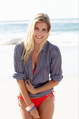 A blonde woman on a beach wearing a red bikini and a blue blouse