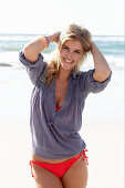 A blonde woman on a beach wearing a red bikini and a blue blouse