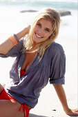 A blonde woman on a beach wearing a red bikini and a blue blouse