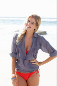 A blonde woman on a beach wearing a red bikini and a blue blouse