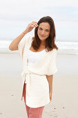 A brunette woman by the sea wearing a short-sleeved cardigan