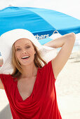 A blonde woman on a beach wearing a red top and a white hat