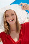 A blonde woman on a beach wearing a red top and a white hat