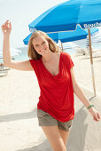 A blonde woman on a beach wearing a red top and shorts