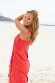 A young blonde woman on a beach wearing a red summer dress